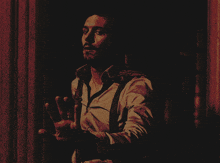 a man in a white shirt and suspenders stands in the dark