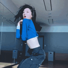 a woman in a blue crop top and black cargo pants is dancing in front of a mirror