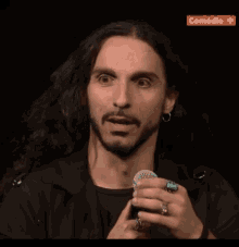 a man with long hair and a beard is holding a microphone in front of a screen that says comedie