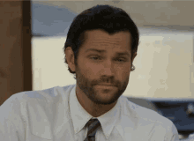 a man with a beard wearing a white shirt and tie looks at the camera