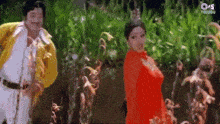 a man in a yellow jacket and a woman in a red dress are dancing in front of trees .