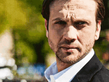 a man with a beard is looking at the camera with a serious look on his face