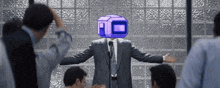 a man in a suit stands in front of a microphone with a purple box on his head ..