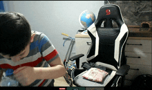 a boy is drinking water from a bottle in front of a gaming chair that has the letter s on it