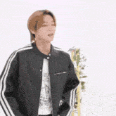 a young man wearing a black jacket with white stripes on the sleeves is standing in front of a white wall .