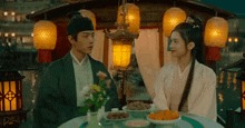 a man and a woman are sitting at a table with lanterns .