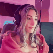a woman wearing headphones and a pink blanket looks to the side