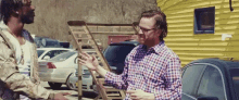 a man in a plaid shirt is talking to another man in front of a yellow building