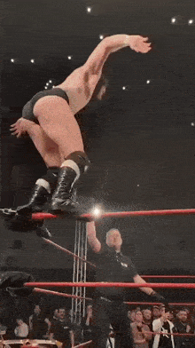 a wrestler is jumping in the air in a wrestling ring while a crowd watches .