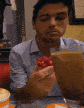 a man in a blue shirt is eating strawberries and drinking a milkshake
