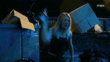 a woman in a black tank top is standing in a dumpster with a max logo in the background