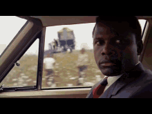 a man in a suit and tie sits in a car looking out the window
