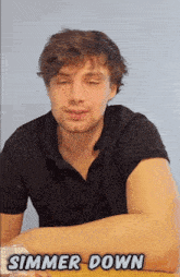 a man in a black shirt is sitting at a table with the words simmer down above him