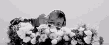 a black and white photo of a man smelling flowers .