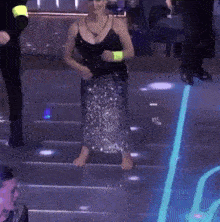 a woman in a sequined skirt is walking barefoot on a dance floor
