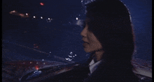 a woman in a black suit and tie stands in front of a car