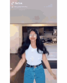a woman is dancing in a kitchen wearing glasses and a white shirt .