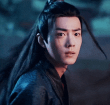 a young man with long hair is wearing a black jacket and looking at the camera .
