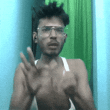 a man wearing glasses and a white tank top is clapping his hands in front of a green curtain .