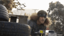 a man with long hair is standing in front of a tire with a comedy central logo visible