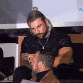 a man with long blonde hair and a beard is sitting next to another man .