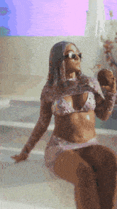 a woman in a bikini and sunglasses is holding a coconut in her hand