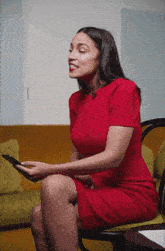 a woman in a red dress is sitting in a chair and looking at her phone