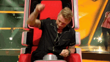 a man in a black shirt is sitting in a red chair with headphones on and pressing a button .