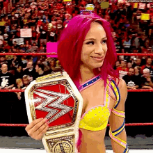 a woman with pink hair is holding a wrestling championship belt in a wrestling ring .