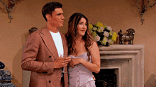 a man and woman standing next to each other in front of a fireplace .