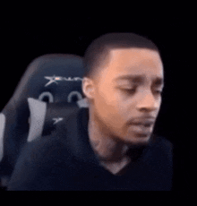 a man is sitting in a gaming chair with his eyes closed and making a funny face .
