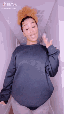 a woman wearing a black sweater and hoop earrings is dancing in a hallway ..