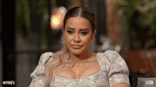 a woman with a tattoo on her chest sits in front of a sign that says # mafs