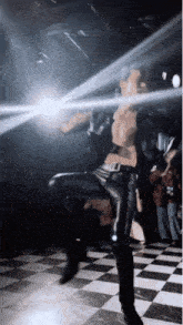 a man without a shirt is dancing on a checkered floor in a dark room
