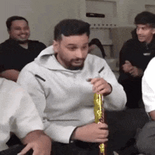 a man with a beard is holding a gold confetti cannon while sitting in front of a group of people .