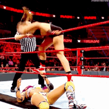 two women are wrestling in a wrestling ring with a referee in the background .