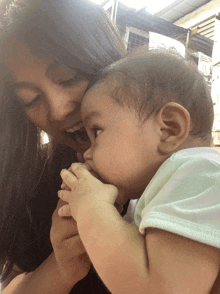 a woman is holding a baby in her arms and the baby is biting her hand