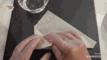 a person folding a piece of paper with a bowl of water in the background and the words made in animotica on the bottom