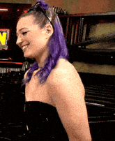 a woman with purple hair is smiling in front of a sign that has the letter w on it