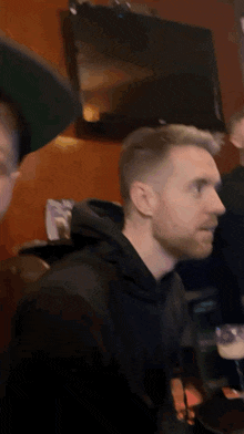 a man with a beard is wearing a black hoodie and looking at the camera .