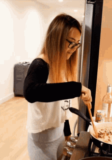 a woman in glasses stirs food in a pan
