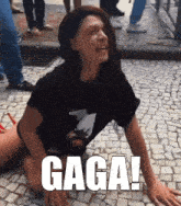 a woman in a black shirt is kneeling on the ground with gaga written in white letters