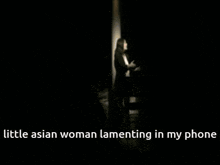 a little asian woman lamenting in her phone in a dark room