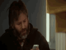 a man with a beard is looking at a cell phone .