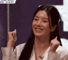 a woman with long black hair is smiling and holding her fist up in the air .