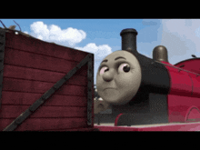 a red train with a cartoon face is standing next to a wooden box