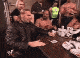 a man in a leather jacket is sitting at a table with a group of men playing cards .