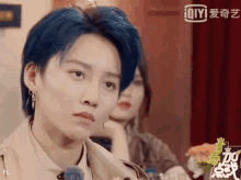 a woman with blue hair is sitting in front of a sign that says iqiyi