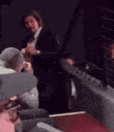 a man in a suit is standing in a dark room with other people