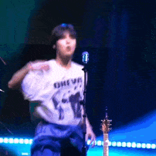 a man in a chevy shirt is singing into a microphone on a stage .
